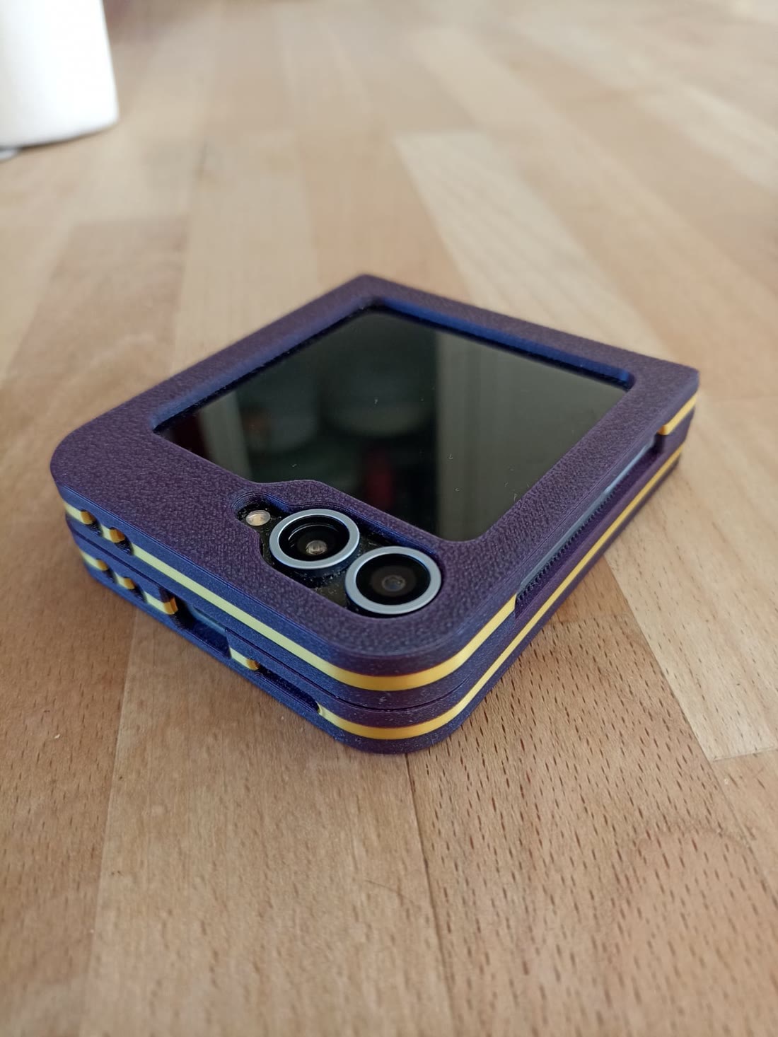 A purple and yellow printed case on a folding phone, closed, on a wooden table.