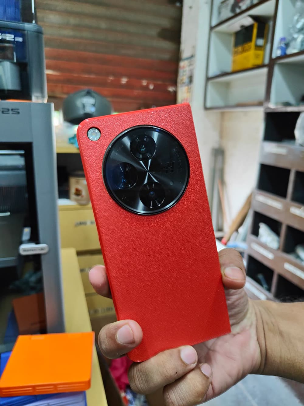 A red textured phone case held in a hand at the shop counter.