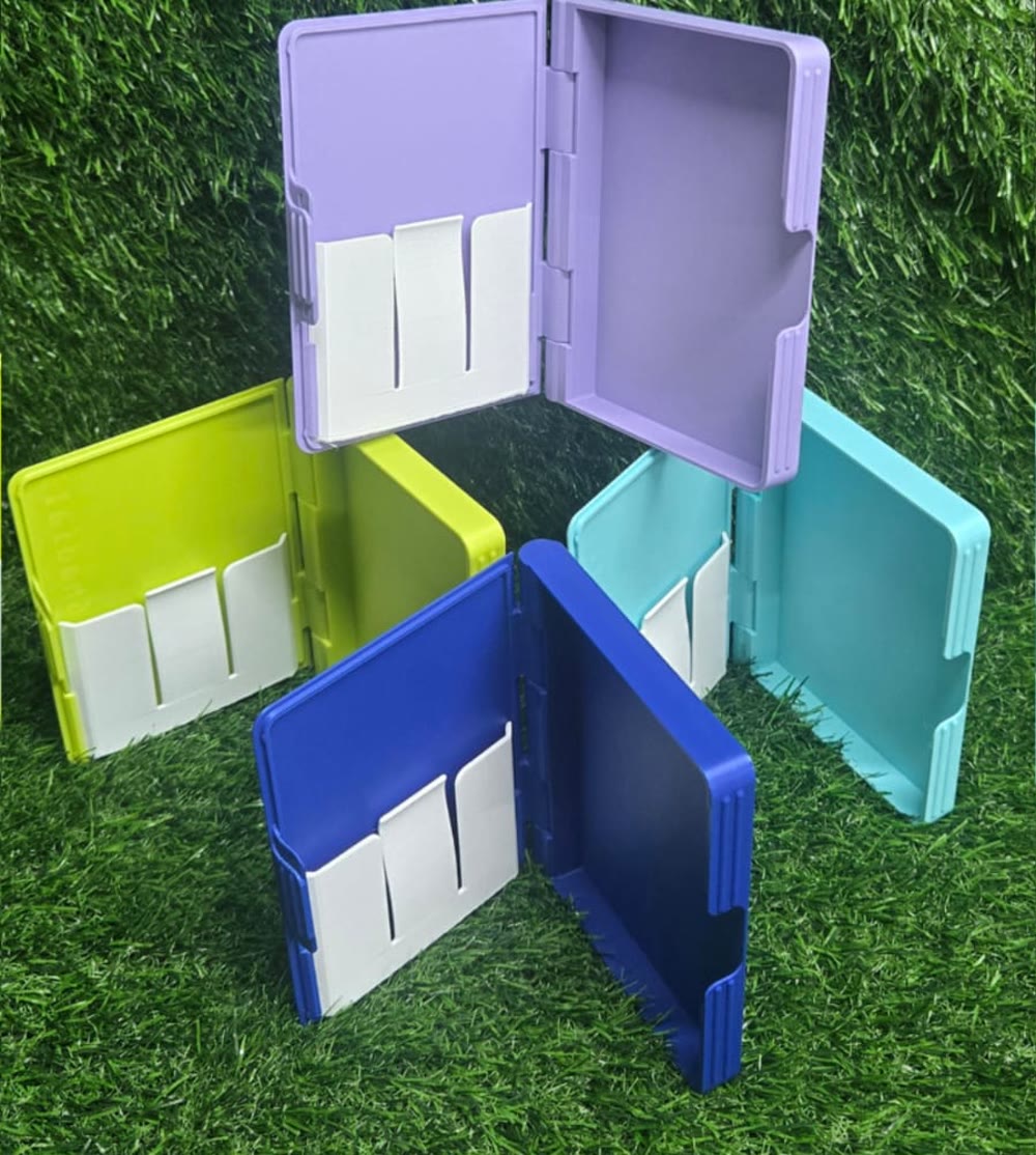Four printed passport and card holders in purple, lime, blue and teal, open on grass.
